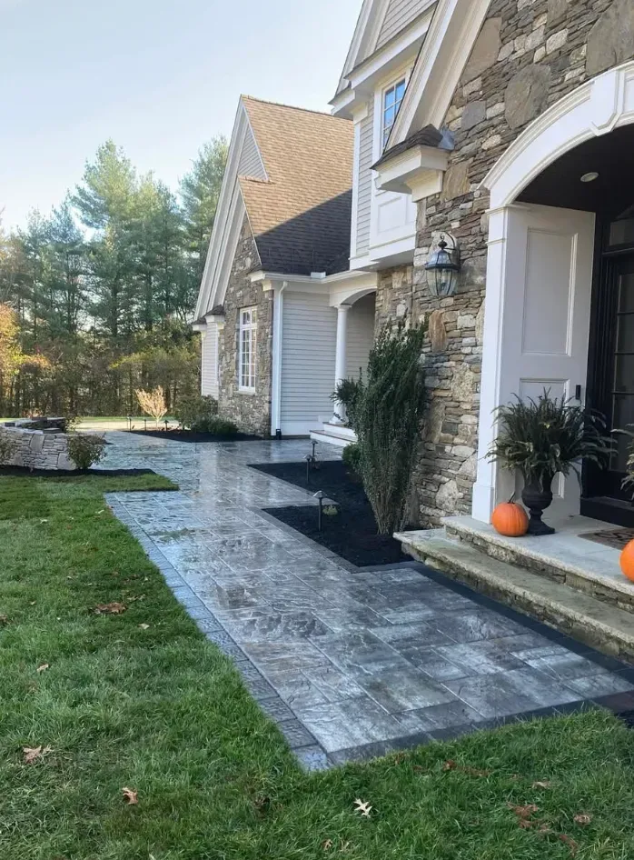 Stone walkway leading to a house with stone and gray siding. Green grass and fall pumpkins.