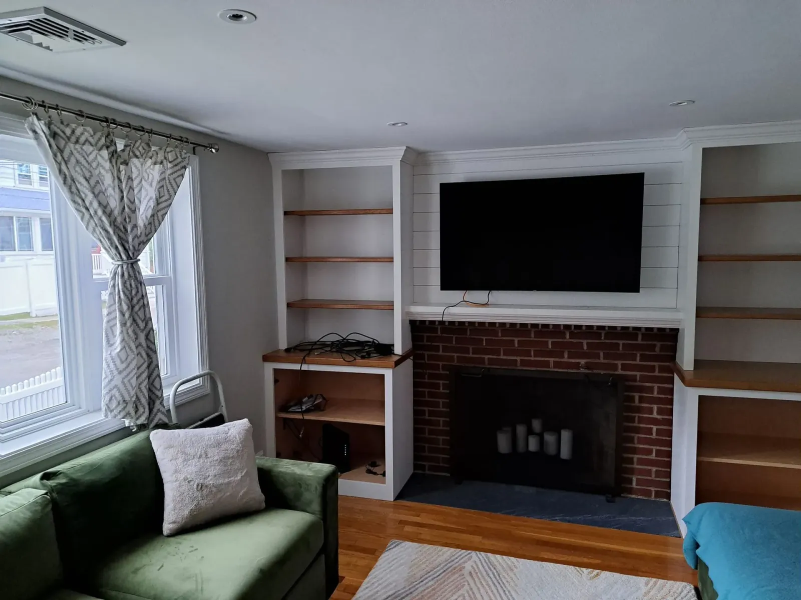 Living room with green sofa, fireplace, built-in shelves, and a TV mounted above the mantel.
