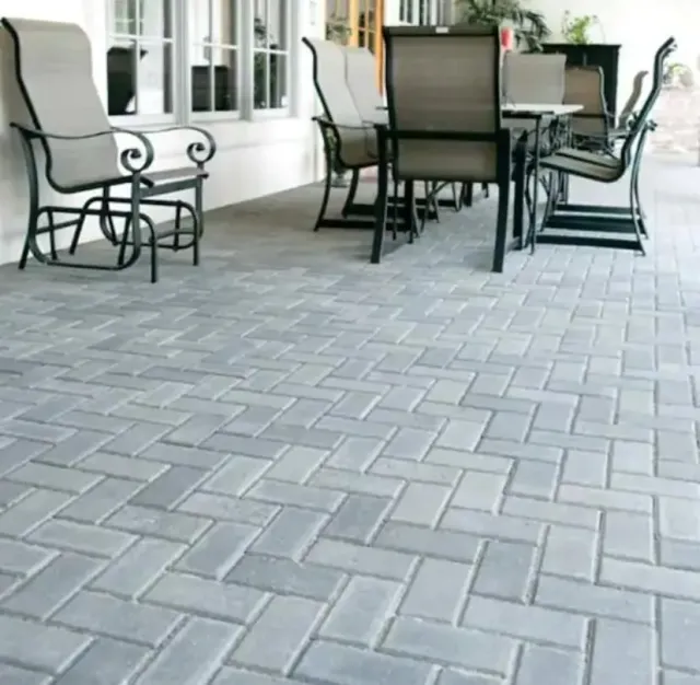 Patio with black metal chairs and table on gray brick pavers beside a white house
