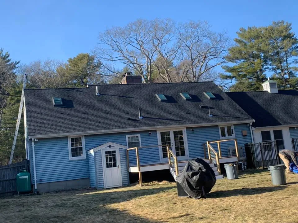 A blue house with a black roof is sitting on top of a lush green field.