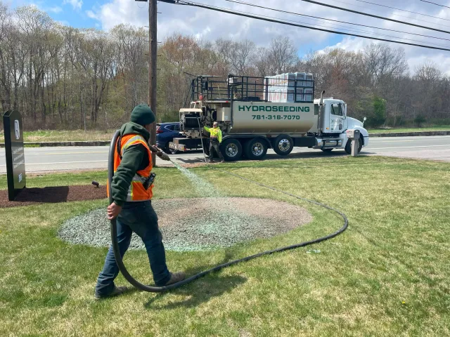 Professional landscaper applying hydroseeding to a commercial lawn in Massachusetts using specialized equipment — Xquisite Landscaping delivering expert grass growth solutions.