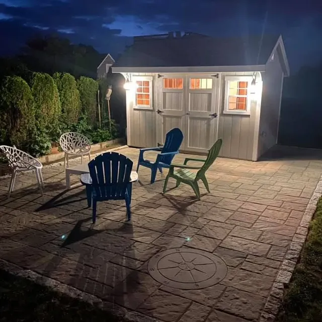 Paver patio with fire-pit seating and outbuilding at dusk