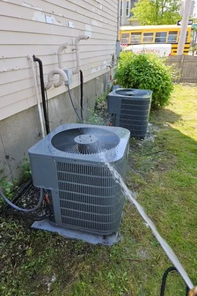 Hose spraying water on outdoor air conditioner