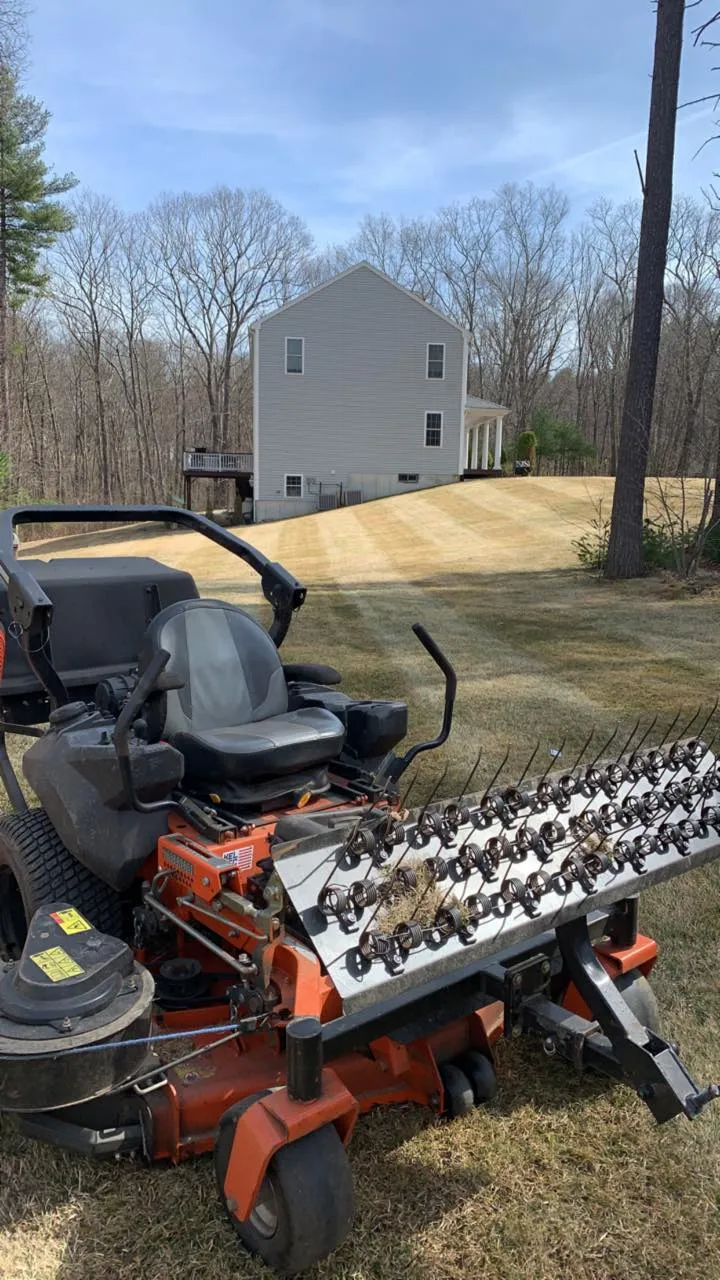A lawn mower is parked in the grass in front of a house.