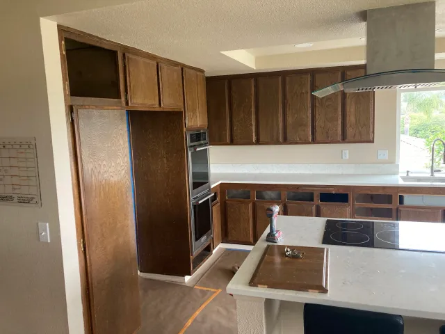 A kitchen with wooden cabinets, a built-in oven, a stove on the island, and a window with greenery outside.