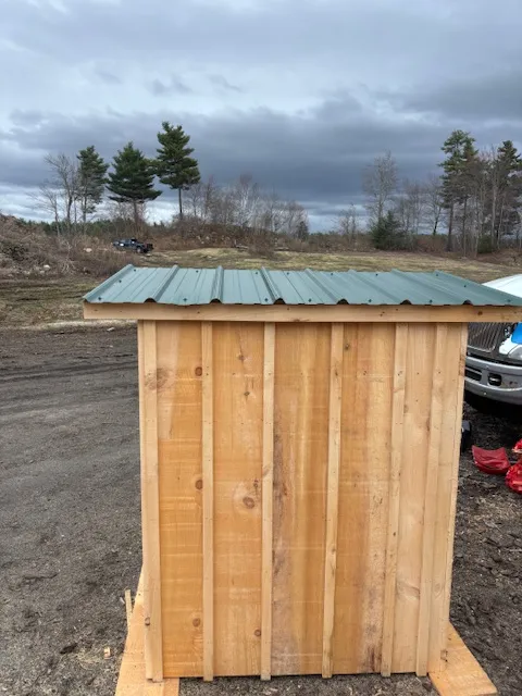 Custom wooden shed with metal roof, showcasing craftsmanship and durable materials, set against a cloudy sky in a rural area.