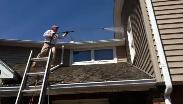 Man up on roof pressure washing the siding Hadley Ma.