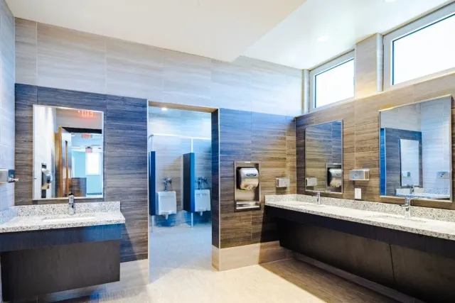 Modern public restroom with gray tiled walls, granite countertops, and stainless steel fixtures.