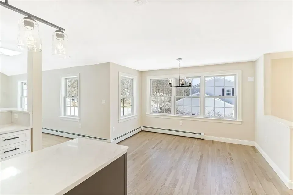 A bright, open dining area with light hardwood floors, neutral walls, large windows, and a modern chandelier.