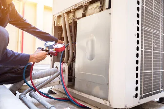 Technician model checking refrigerant pressure on residential cooling equipment