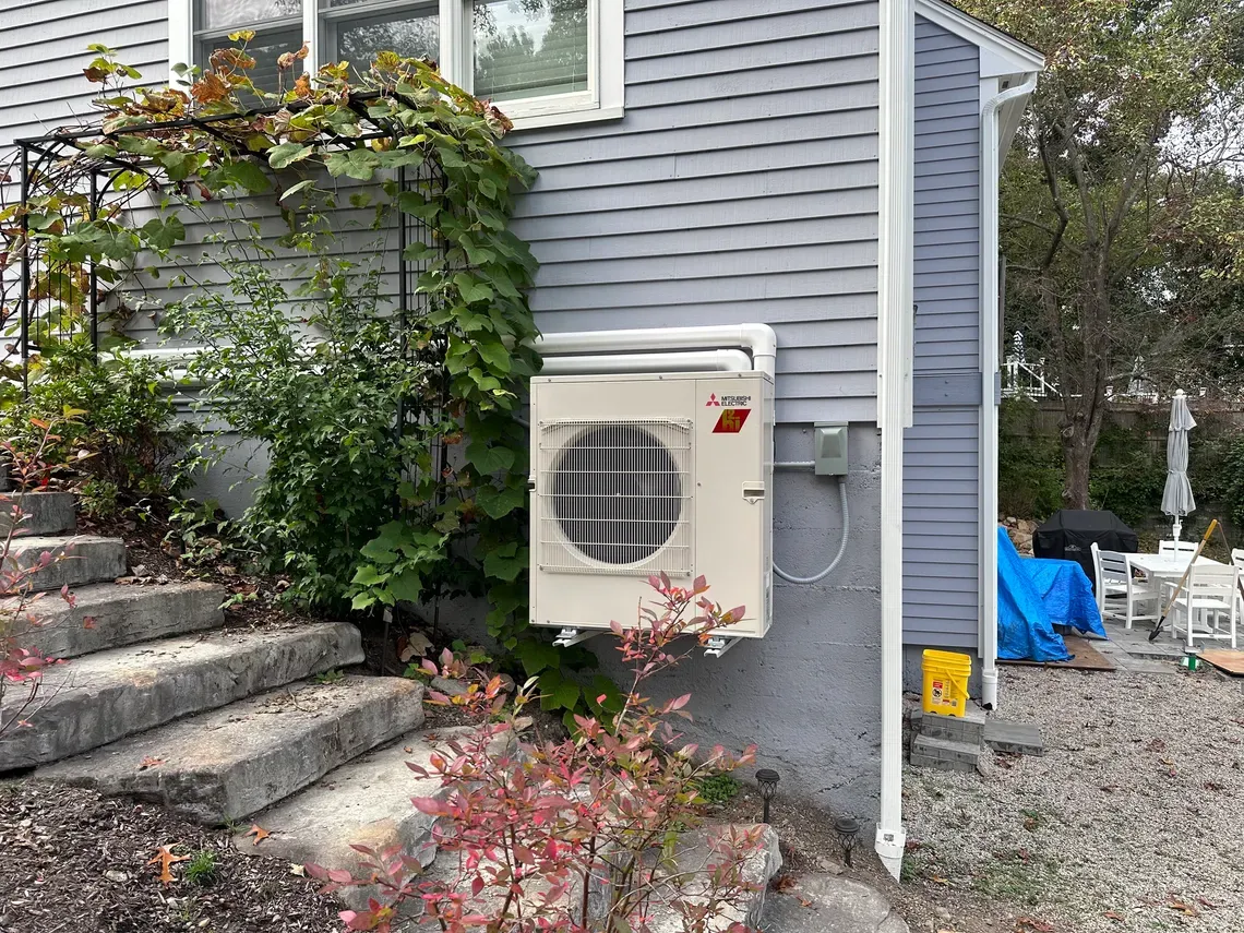 A white air conditioner is mounted on the side of a house.