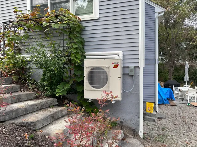 A white air conditioner is mounted on the side of a house.