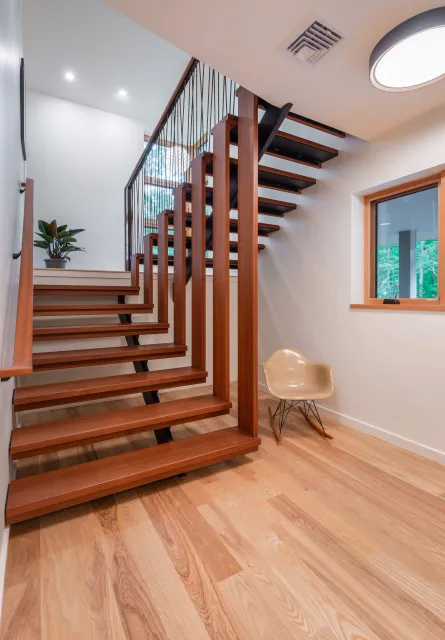 Interior of a modern home with wooden stairs, light wood floors, original Eames rocking chair and warm recessed lighting.