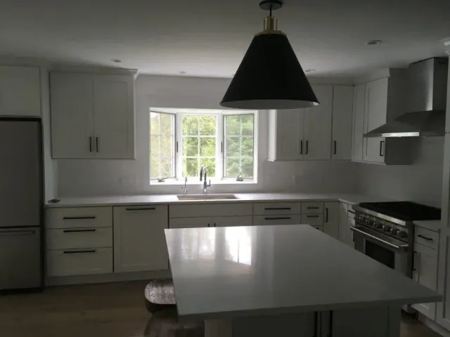 Bright white kitchen with island, cabinets, window over sink, and black pendant light.