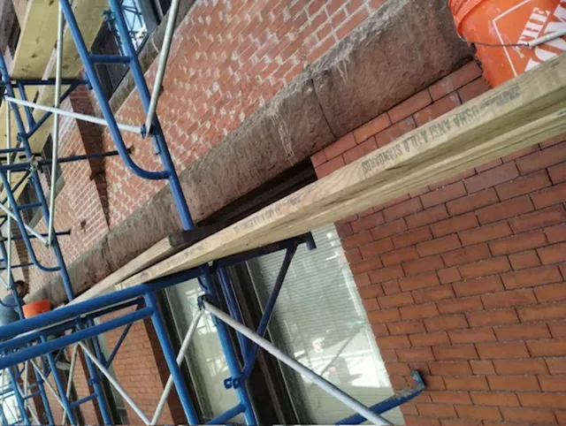 A bucket sits on the side of a brick building