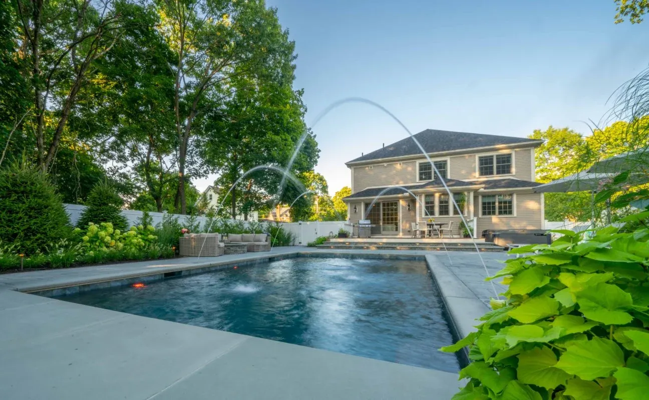Backyard pool with water features, tiered patio, and lush landscape design in Westwood, Massachusetts by Land Design Associates.