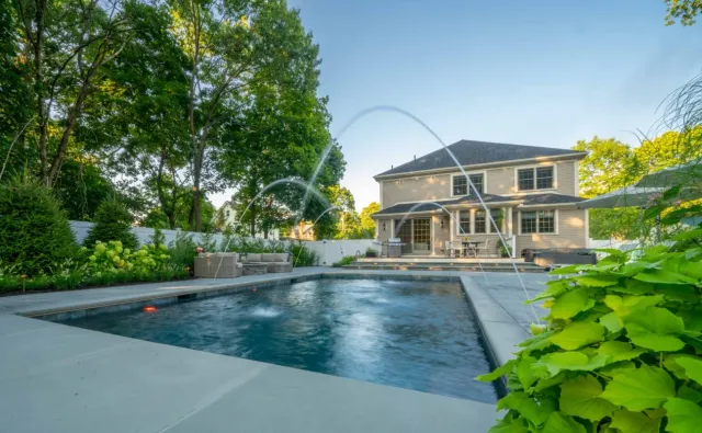 Backyard pool with water features, tiered patio, and lush landscape design in Westwood, Massachusetts by Land Design Associates.
