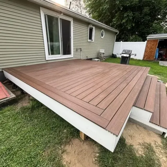 Composite deck beside a house with brown planks, white trim, and grassy yard underneath