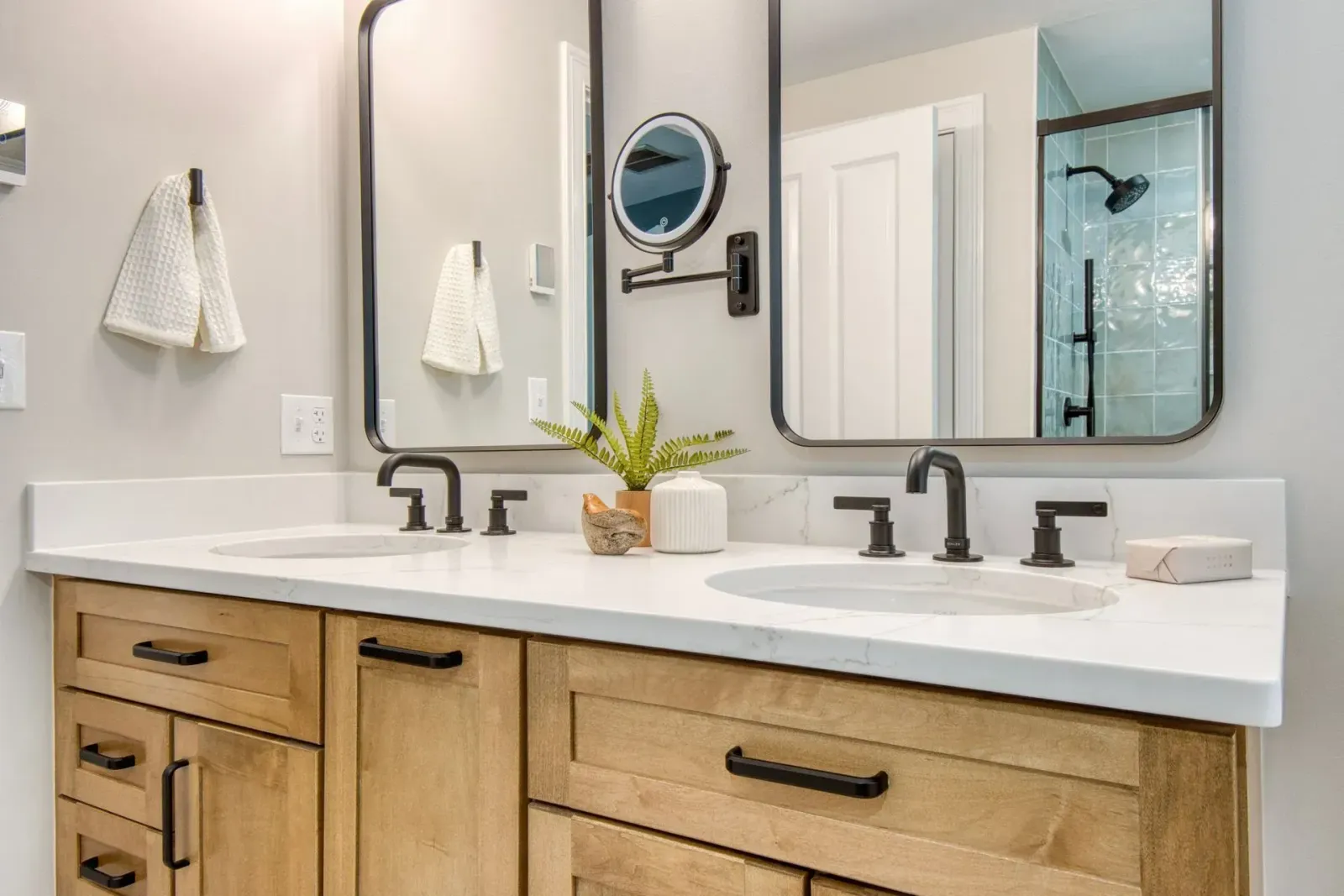 Modern bathroom vanity with double sinks, black fixtures, wood cabinets, and mirrors