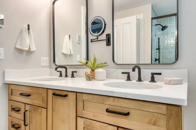 Modern bathroom vanity with double sinks, black fixtures, wood cabinets, and mirrors