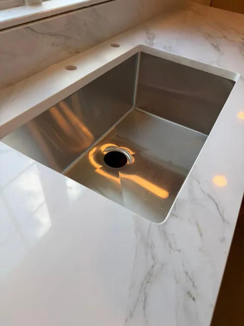 Stainless steel kitchen sink set in a white marble countertop with a faucet hole visible.
