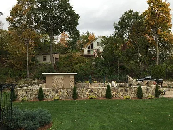 A stone wall surrounds a lush green lawn in front of a house.