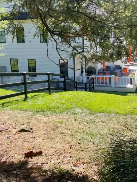 Backyard with white house, wooden deck, green grass, and a black fence.