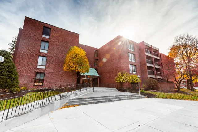 Red brick apartment building with trees in fall colors and a bright sky with the sun shining.