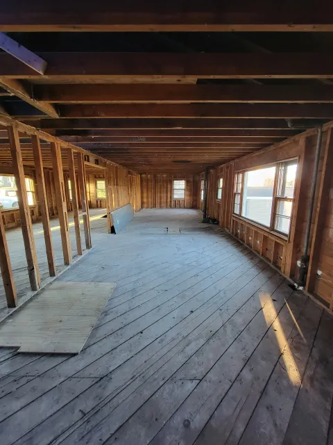 Interior of a house under renovation with exposed wooden framing, large windows, and a wooden floor.