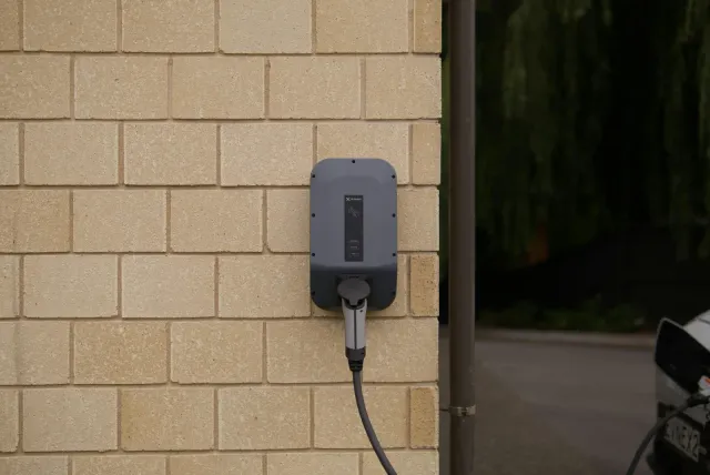 Electric vehicle charger mounted on a brick wall with a charging cable connected.
