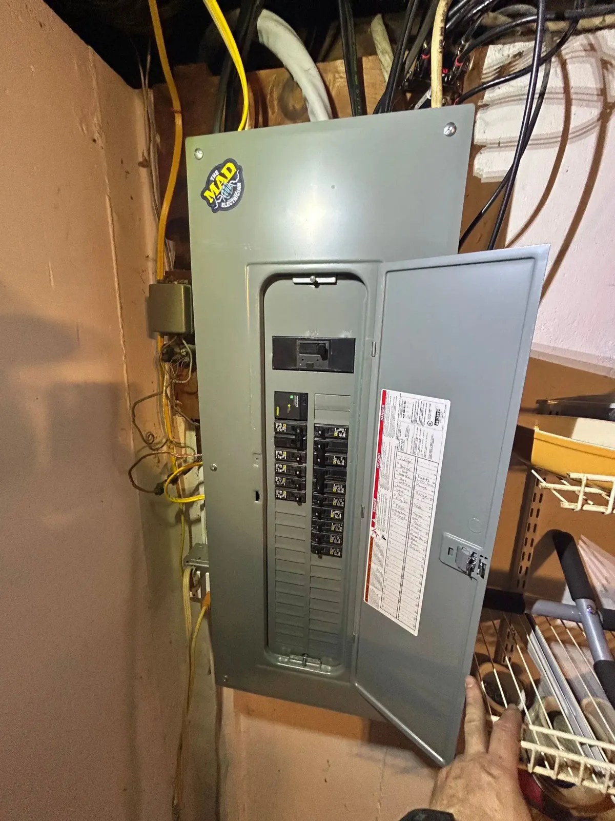 Open electrical breaker panel with exposed wiring in a utility closet