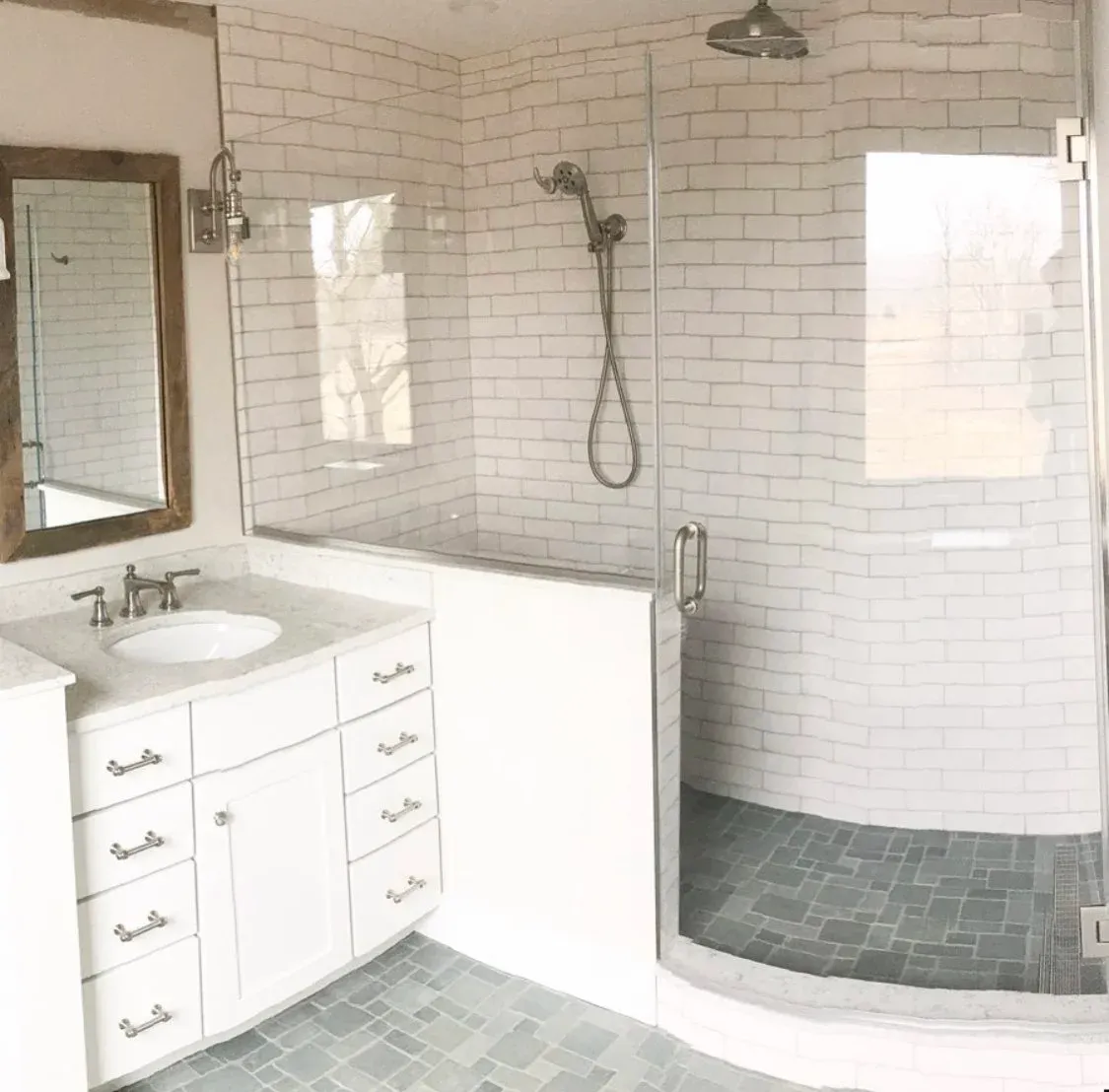 Modern bathroom with a white vanity, round sink, wall-mounted mirror, and a glass-enclosed shower with subway tiles.