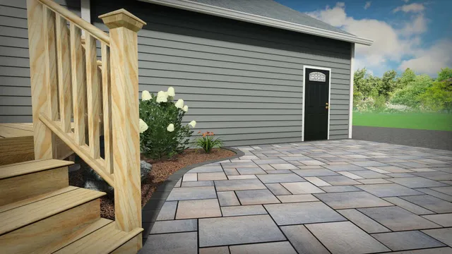 A wooden staircase with a railing leads down to a patterned stone patio outside a grey-sided house with a black door.