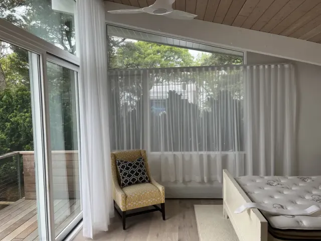 Custom-installed sheer vertical draperies and window treatments in a modern Wellfleet bedroom overlooking a wooded deck.