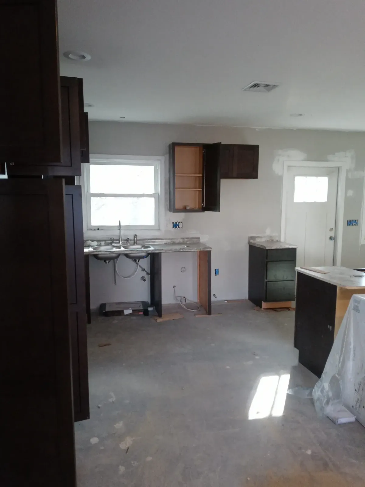 Empty kitchen under renovation with unfinished cabinets, sink, and scattered construction materials