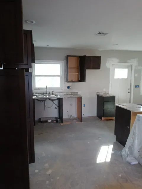 Empty kitchen under renovation with unfinished cabinets, sink, and scattered construction materials