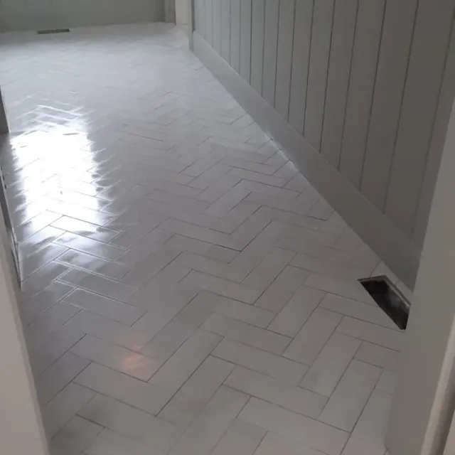 Glossy white herringbone tile floor along shiplap wall by Link Services Pro in Westborough, MA