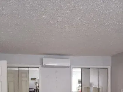 Bedroom with a wall-mounted air conditioner above sliding closet doors and a mirrored wardrobe.