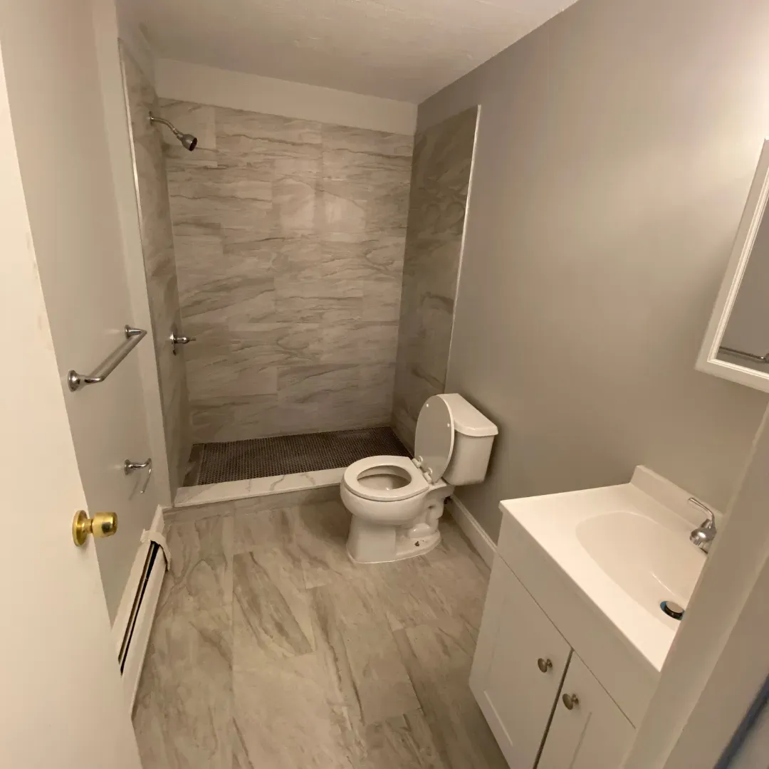 Full bathroom remodel with wood-look stone shower, white vanity and tiled floor by SF Construction in Sudbury, MA