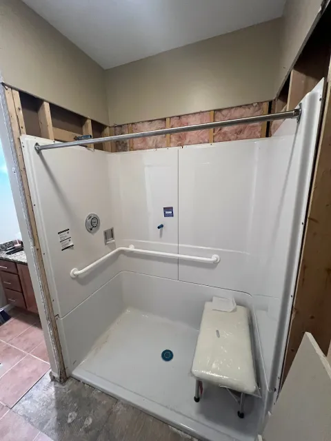 Accessible shower stall with grab bars, built-in seat, and handheld shower in a bathroom