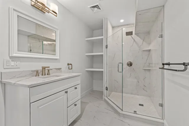 Modern white bathroom with a marble vanity, a large mirror, and a glass-enclosed shower with marble walls.