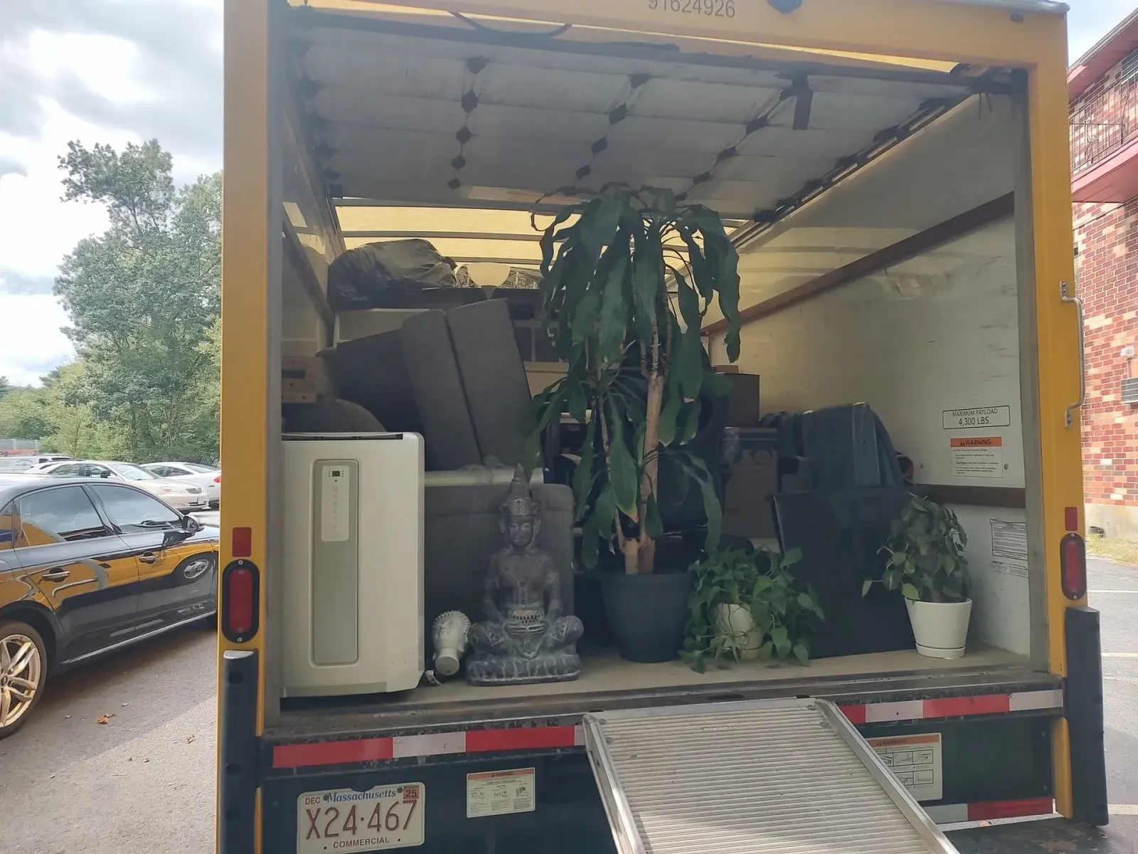 Open moving truck packed with furniture, plants, and household items on a street.