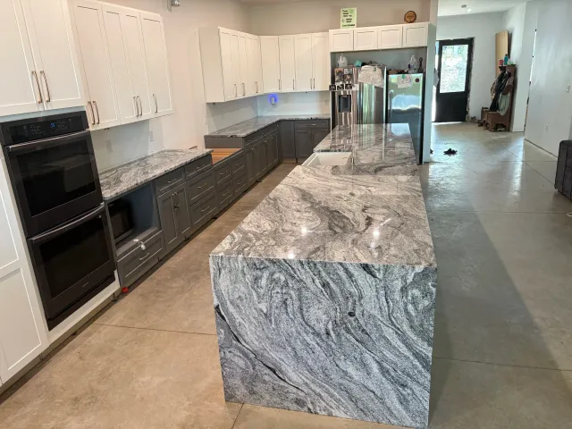 Modern kitchen with gray and white cabinets, granite countertops with gray swirls, and stainless steel appliances, including an oven, microwave, and refrigerator.