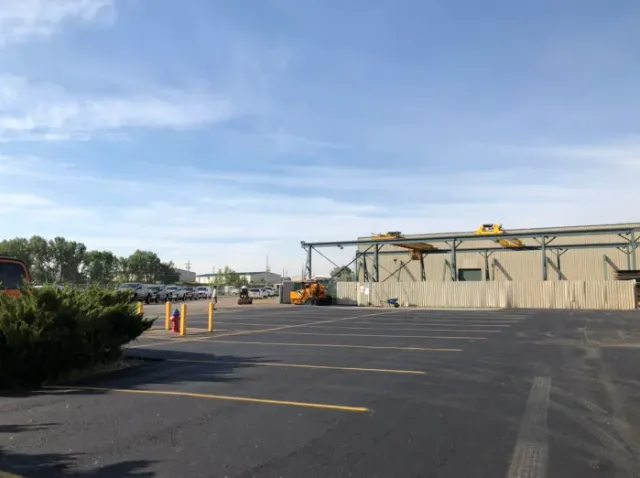 Empty parking lot beside a beige industrial building under a blue sky, with construction equipment nearby