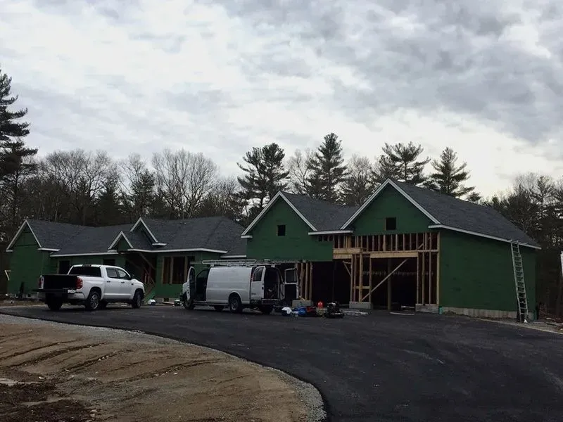 House under construction with framing and roofing complete, vehicles parked on driveway.