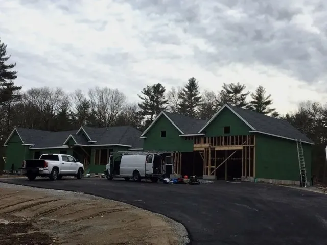 House under construction with framing and roofing complete, vehicles parked on driveway.