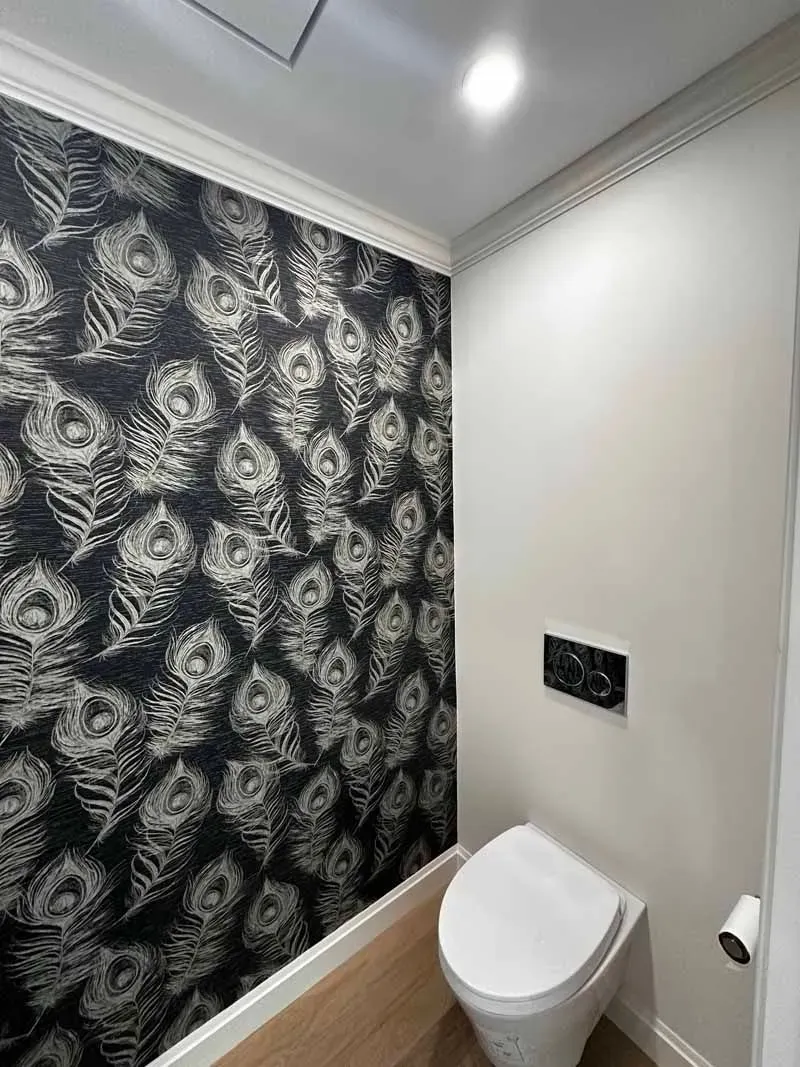 Small bathroom with a toilet and patterned wallpaper. White trim and walls.