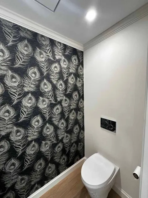 Small bathroom with a toilet and patterned wallpaper. White trim and walls.