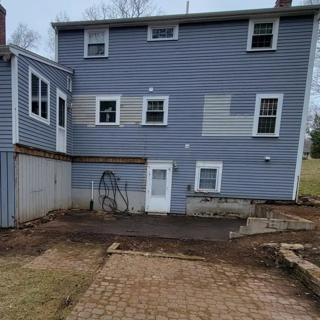 Backyard with newly paved area and construction in progress, house with exterior siding, multiple windows, and a small door.
