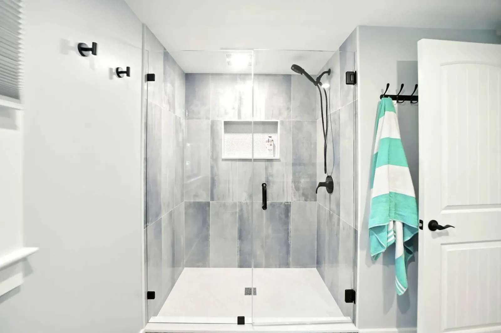 Modern bathroom with tiled shower, bench, towel hook, and open door